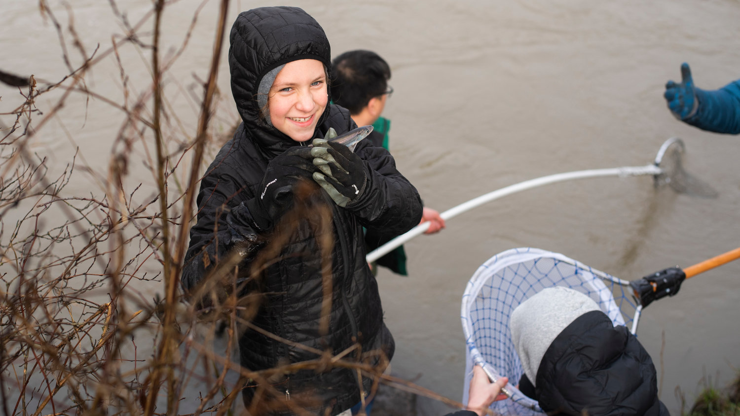 Mirabel Burger, 10, smiles and holds up a smelt scooped up from the Cowlitz River by net alongside family members and other anglers Saturday morning in Castle Rock.