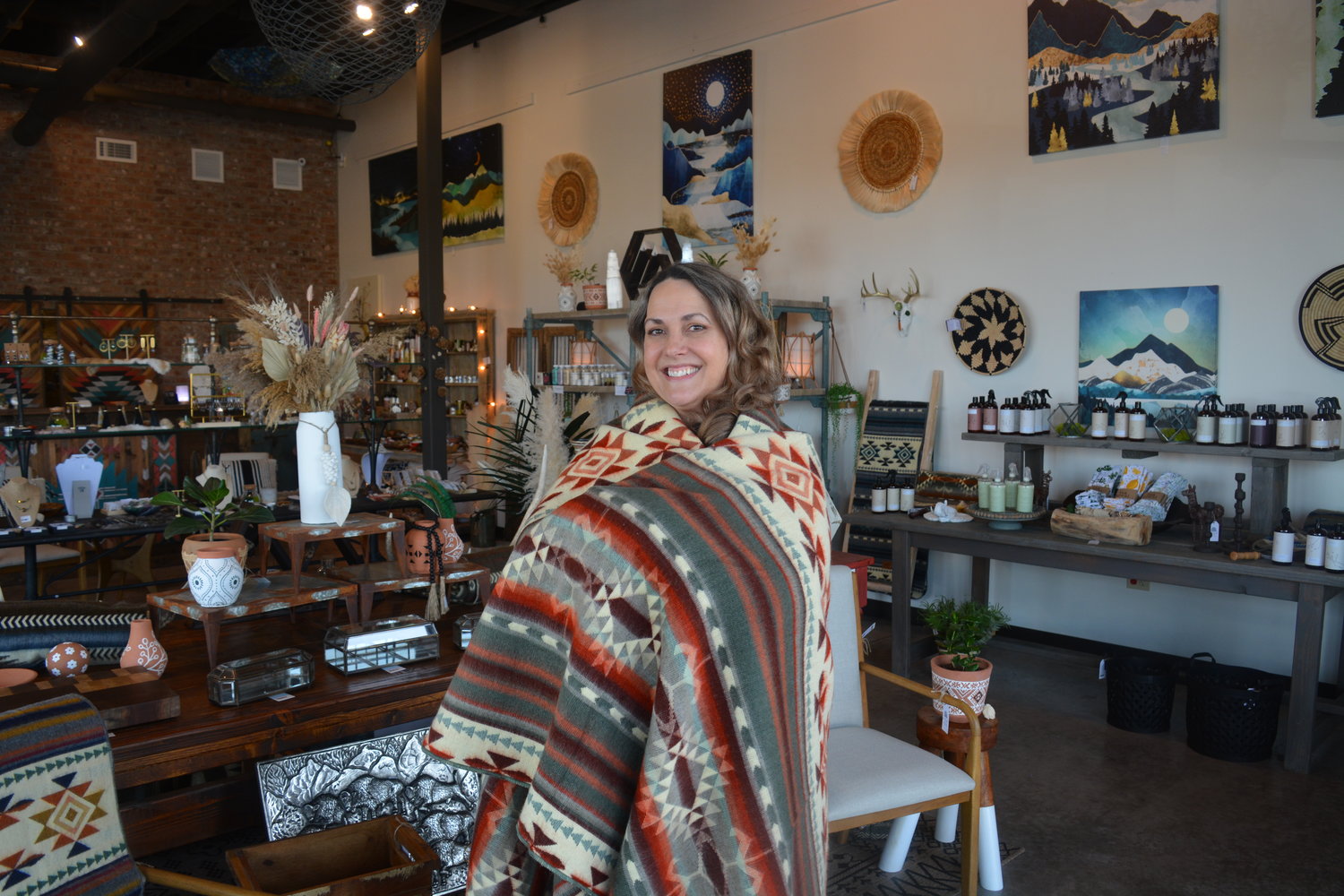 Sara Darden, owner of Native Nomad Home & Gifts, wears a blanket from Heartprint Threads on March 24, which she sells in her shop. The blanket is made of recycled acrylic and one blanket is donated to a family in need for every blanket sold.