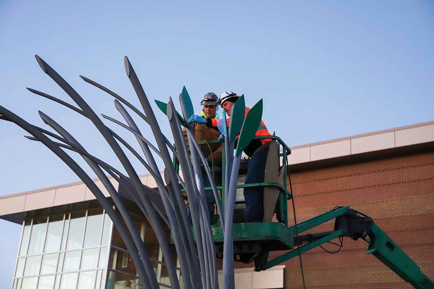 Battle Ground artist Curtis Pittman, left, alongside his fabricator and father-in-law Harold Combs, install the leaves of Pittman’s latest work at Ridgefield High School on Nov. 16.