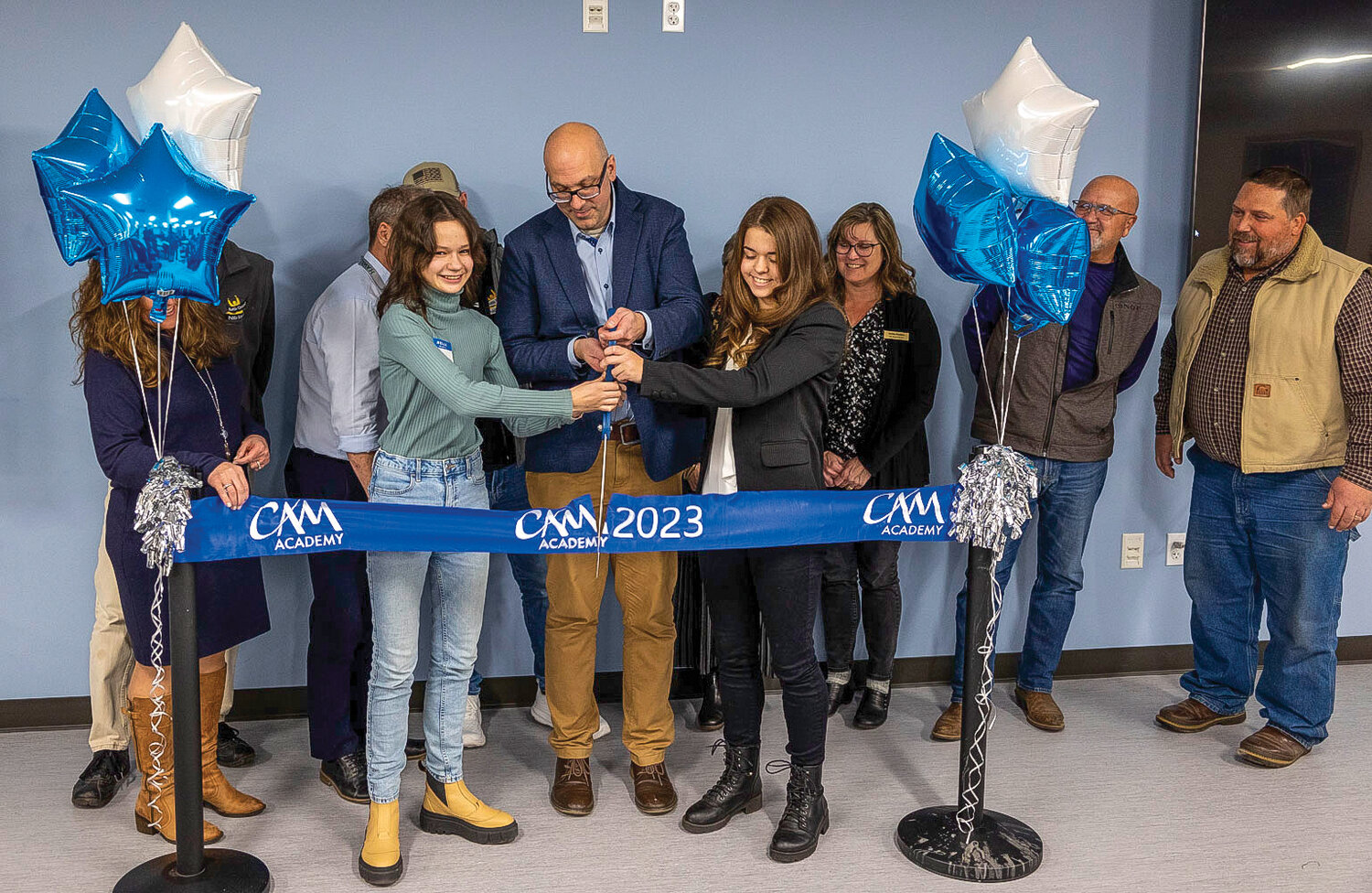 CAM Academy eighth grader Anastasia Royenko, left, and 11th grader Elsa Bice, right, cut the ribbon with Principal Ryan Cowl during the dedication ceremony on Monday, Nov. 27.
