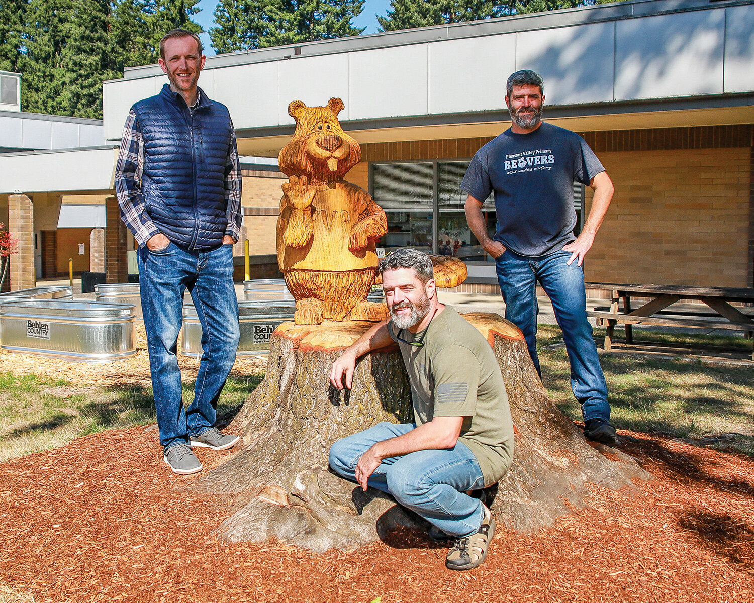 Pleasant Valley School Principal Craig Pearson stands with wood-carving twins Patrick and Mike Bryson with their piece, Buddy the Beaver.