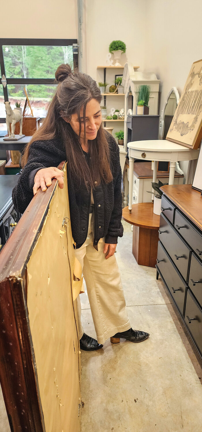 Andrea Hoffman holds back an antique mirror to show one of her dressers, painted in black with the original wood counter.